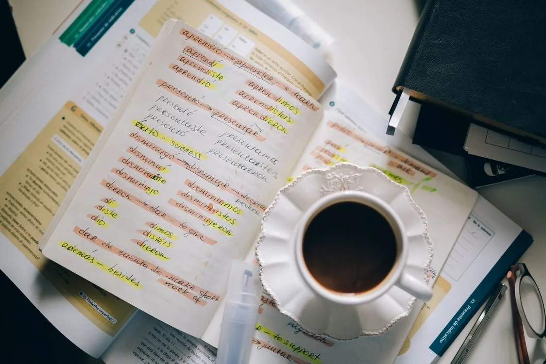 A cup of coffee resting on a notebook page filled with handwritten foreign-language vocabulary notes.